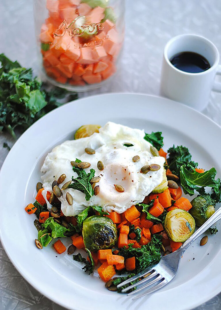 White bowl of sweet potato hash with over-easy eggs, seeds, and kale