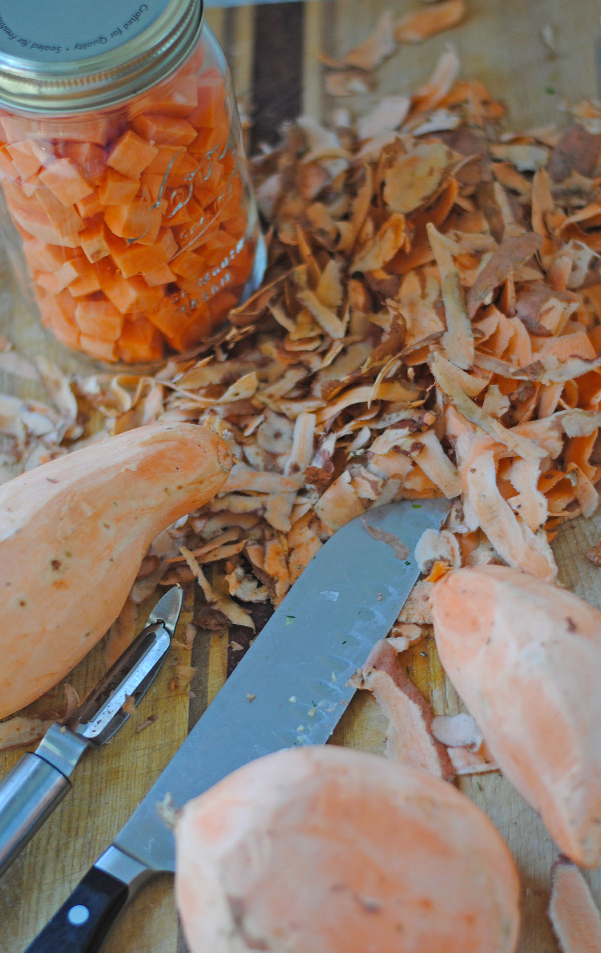 Prepped sweet potatoes in a mason jar on cutting board with peels