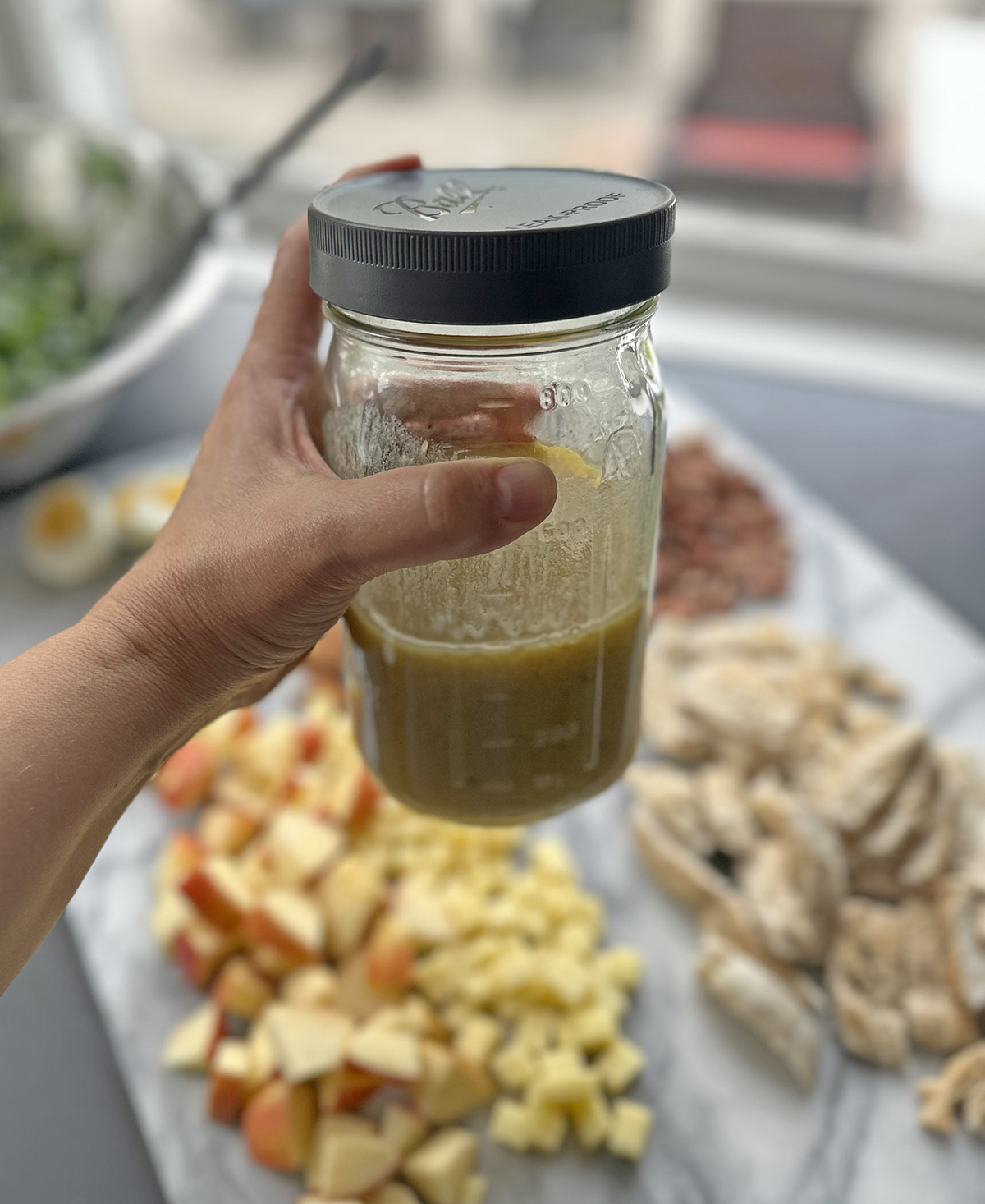 Hand holding a mason jar of homemade honey mustard vinaigrette with salad ingredients in the background