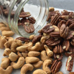 Toasted pecans and cashews spilling from a glass jar onto a marble surface, ready for salad topping
