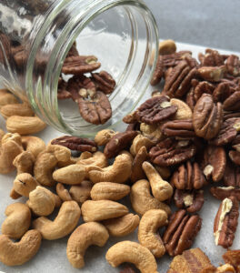 Toasted pecans and cashews spilling from a glass jar onto a marble surface, ready for salad topping