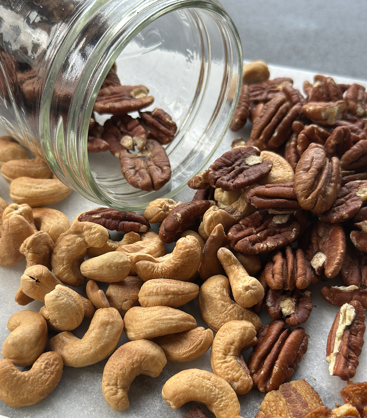 Toasted pecans and cashews spilling from a glass jar onto a marble surface, ready for salad topping