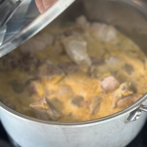 hand opening lid to simmering pork pieces in broth of orange juice