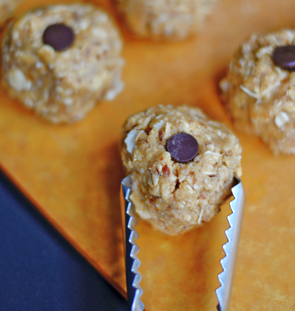 Oat and nut butter energy bite with a chocolate chip on top, held with tongs – no-bake protein snack recipe