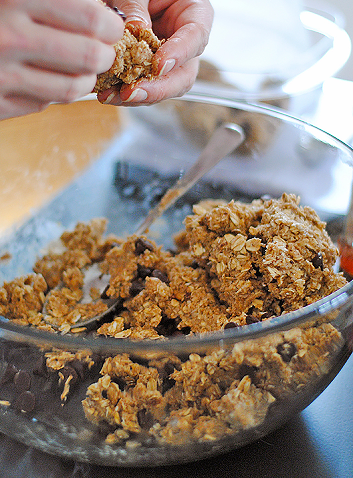 Hands shaping oat and nut butter energy bites from a mixing bowl with oats and chocolate chips – step-by-step protein snack recipe.