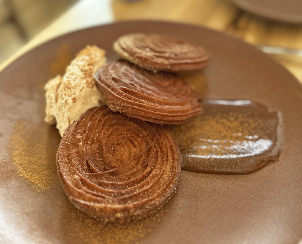 Gluten-free churros with cinnamon whipped cream and dulce sauce on a brown plate at Colita, a 100% gluten-free restaurant in Minneapolis