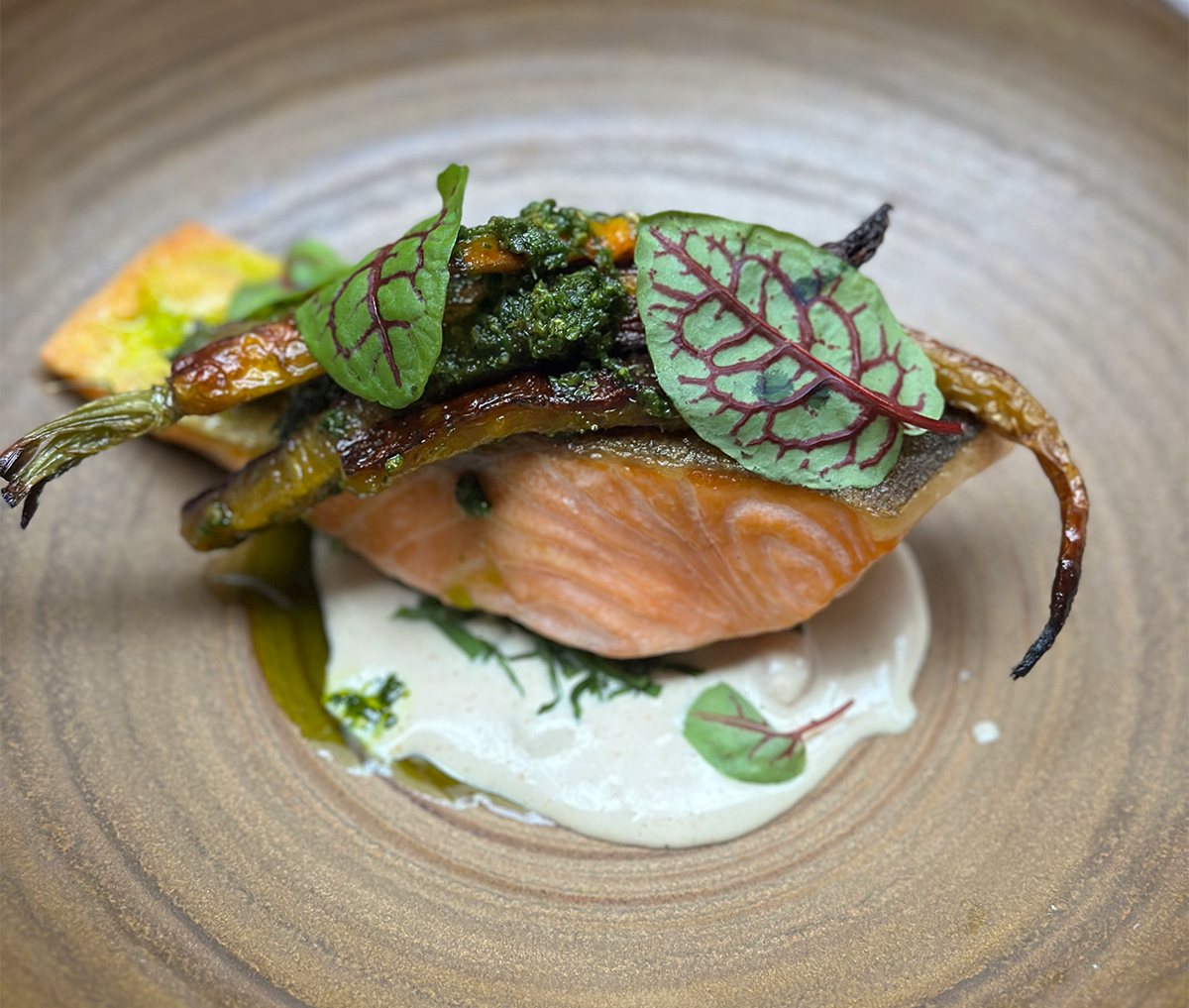 Close-up of seared salmon with crispy skin topped with greens and vegetables at Spoon and Stable in Minneapolis.
