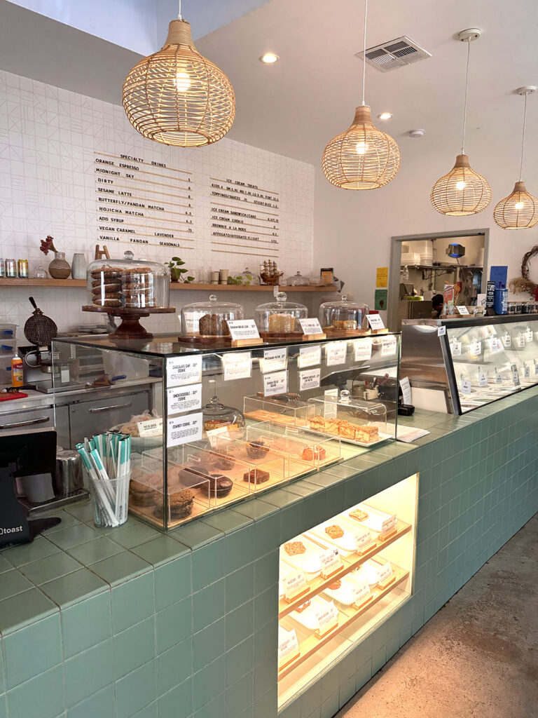 Pastry case filled with gluten-free baked goods under rattan pendant lights at Gati Cafe in Austin